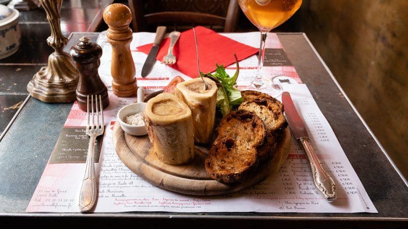 Des os à moelle servis sur une planche avec du pain grillé et un verre de bière ambrée